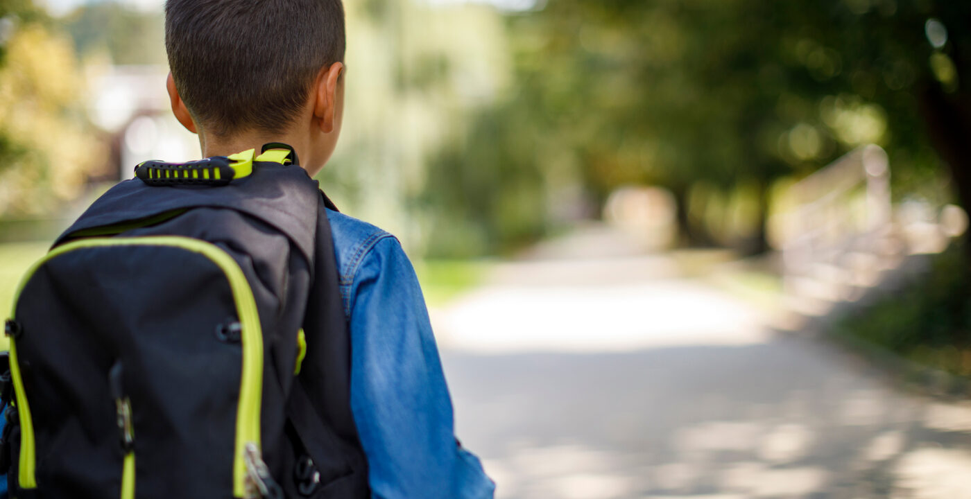 A child is seen from the back walking alone with a backpack on