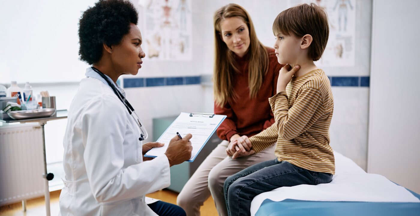 Doctor talks to child, who is touching his throat, and his mother