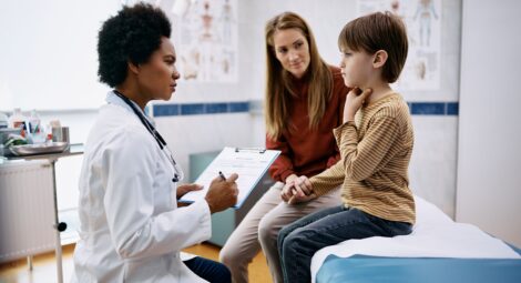 Doctor talks to child, who is touching his throat, and his mother