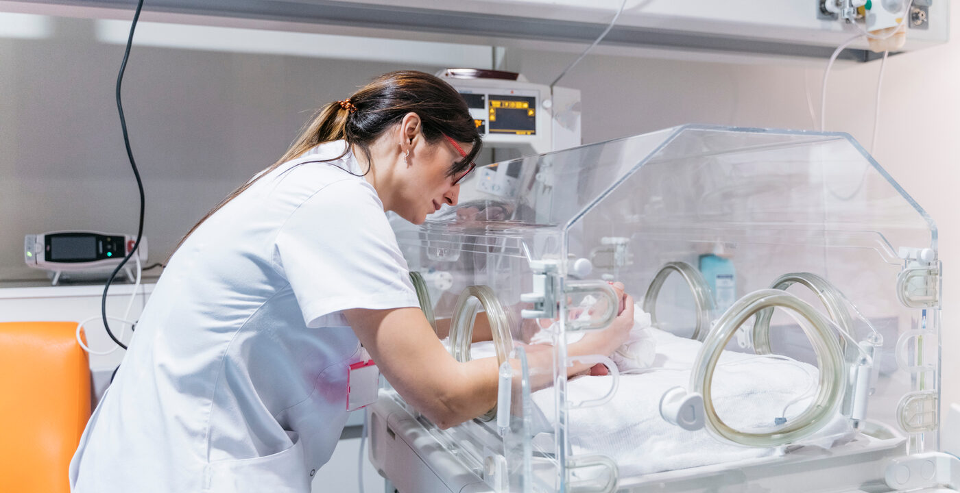 Nurse reaches hands inside of incubator to care for baby