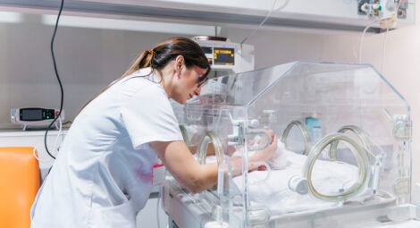 Nurse reaches hands inside of incubator to care for baby