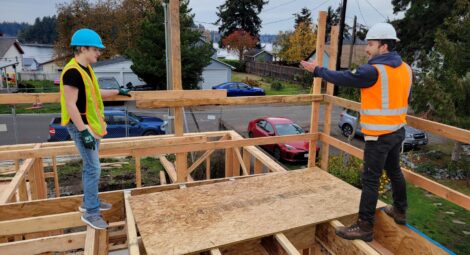 Two people stand on second floor framing of home under construction