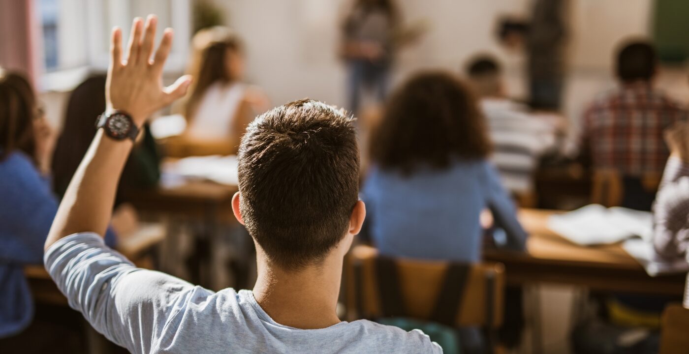 Student in classroom with their hand up, seen from the back