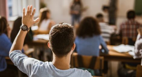 Student in classroom with their hand up, seen from the back