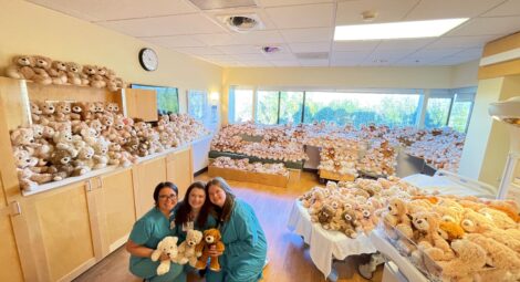Three health care workers hold teddy bears in room filled with teddy bears