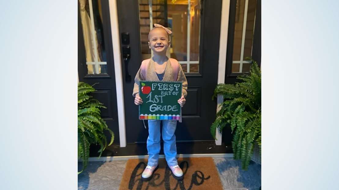 Young girl standing on doorstep holding a sign that says “first day of 1st grade”