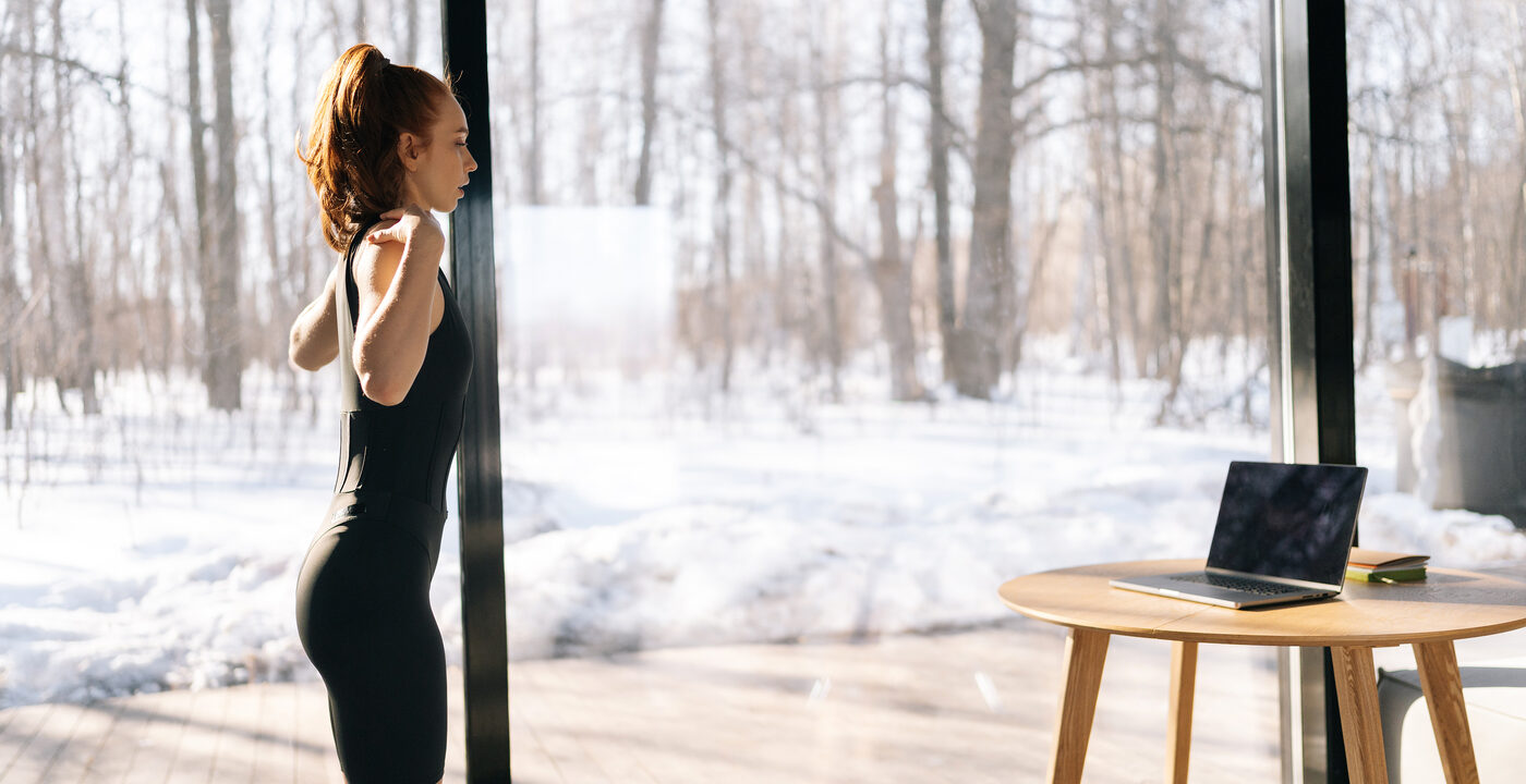 Woman working out inside with a snowy window outside.