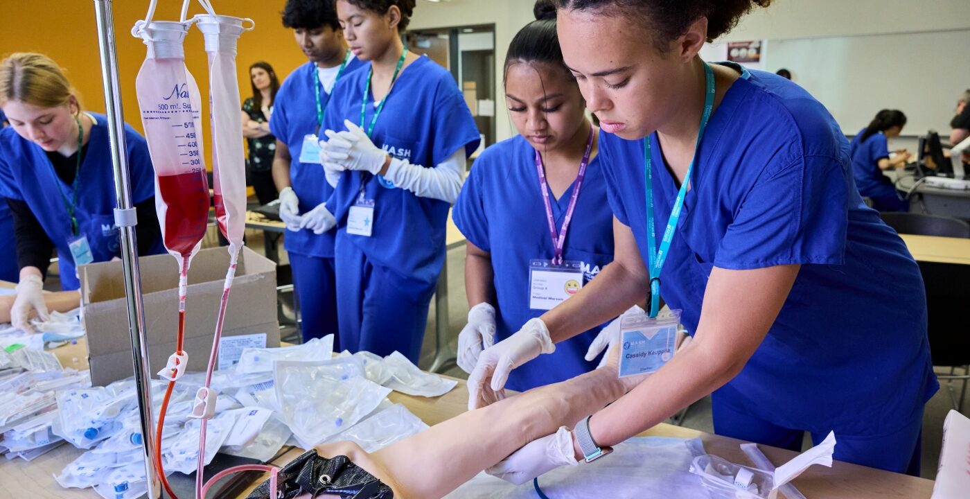 Students in scrubs examine fake arm