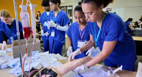 Students in scrubs examine fake arm