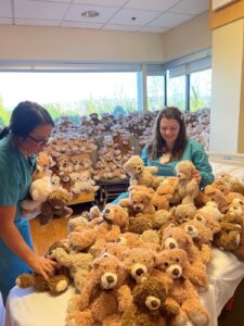 Two health care workers in scrubs organize teddy bears on a table