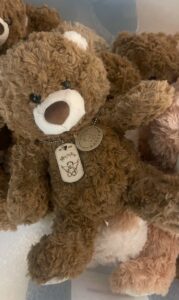 Close-up of brown teddy bear wearing a “Teddies for Tinies” tag on a chain around its neck