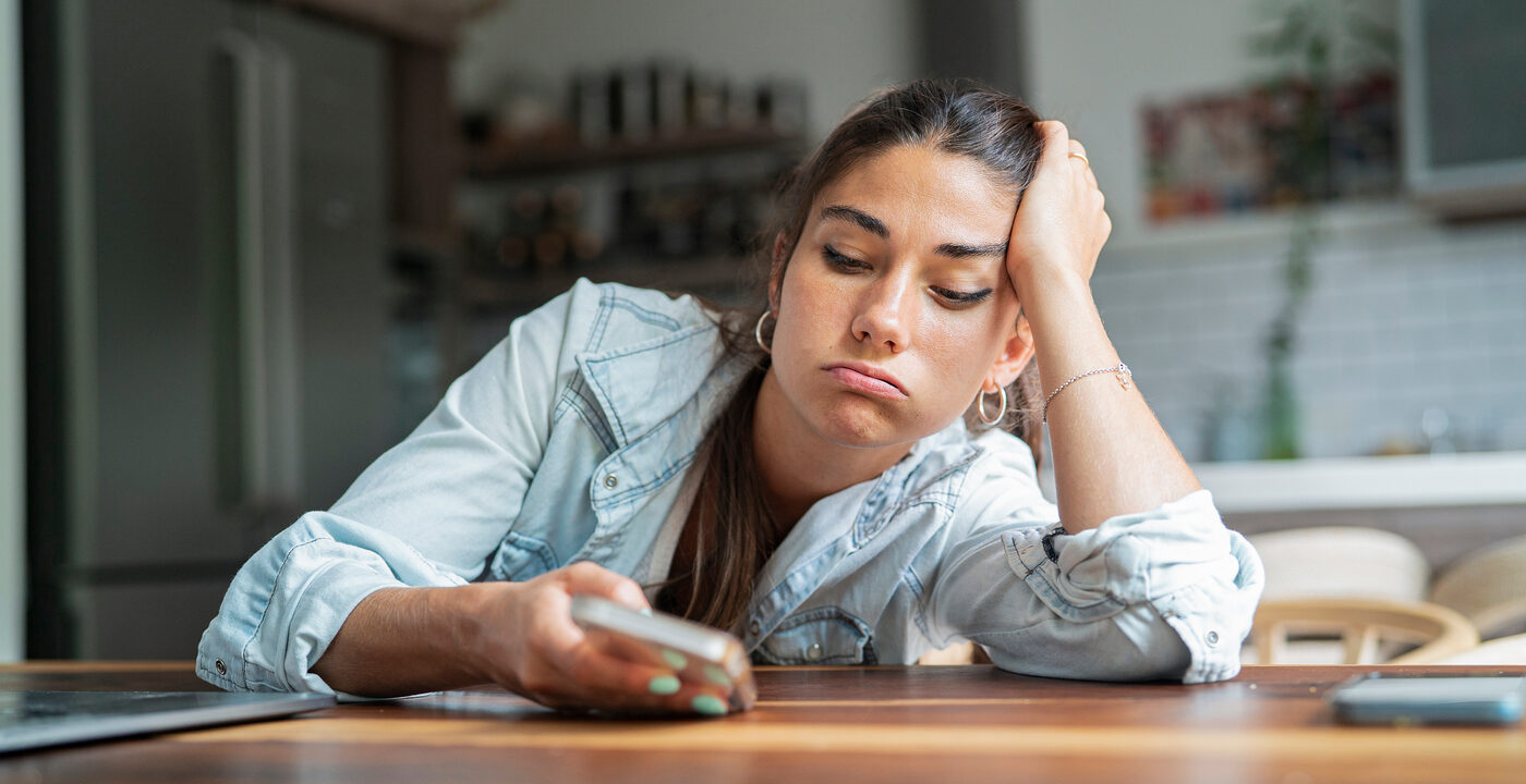 tired woman leans on table and looks at phone