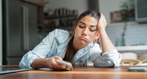tired woman leans on table and looks at phone