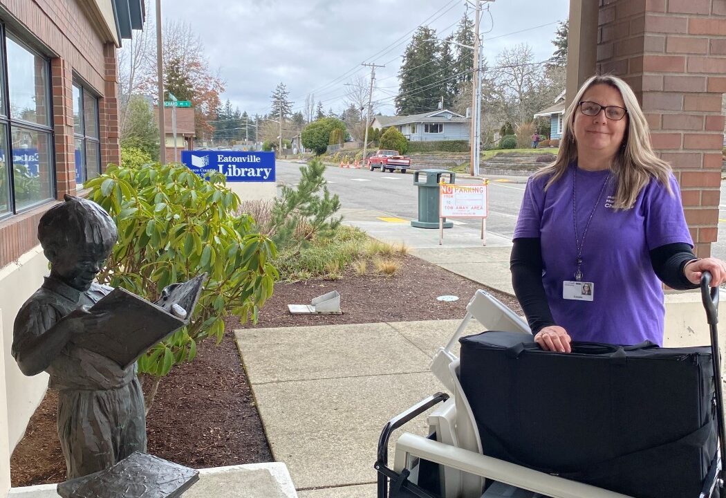 Woman stands in front of Eatonville Public Library with a wagon full of supplies
