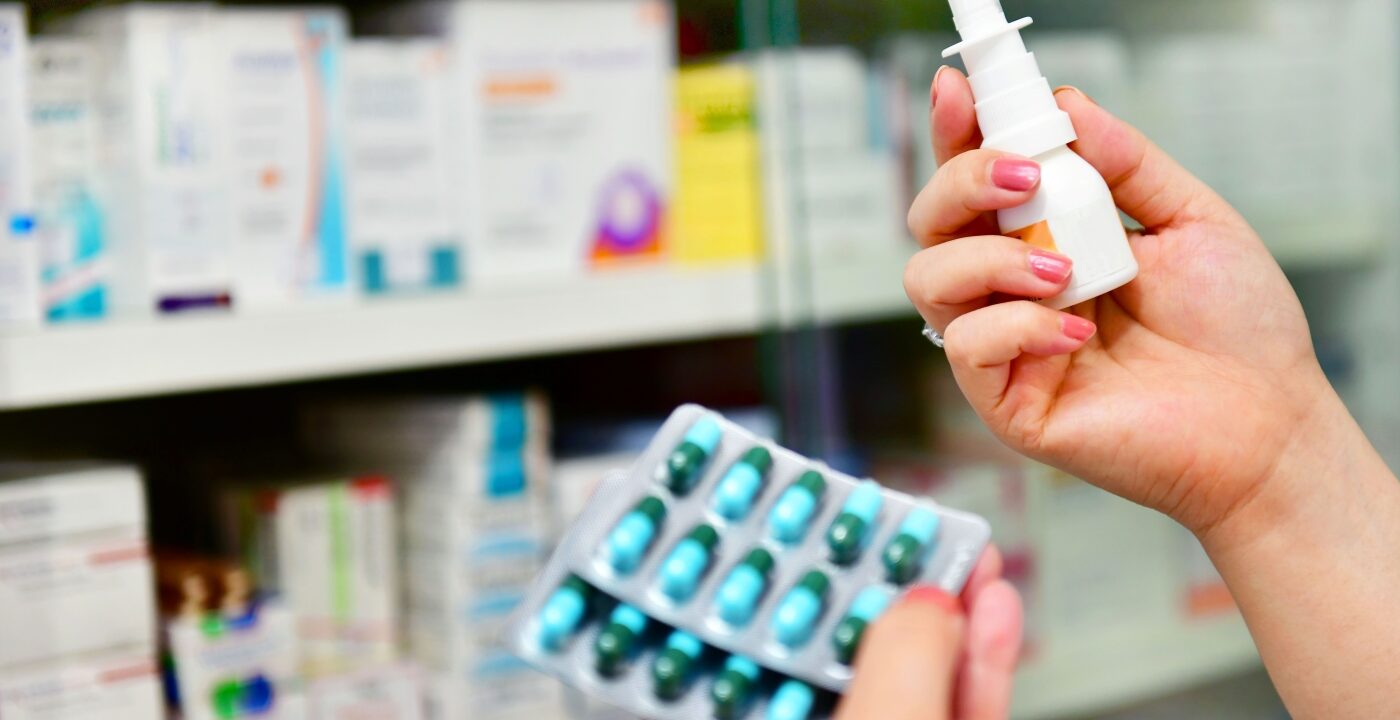 Person in a drugstore aisle holding two different types of allergy medication in their hands