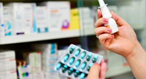 Person in a drugstore aisle holding two different types of allergy medication in their hands