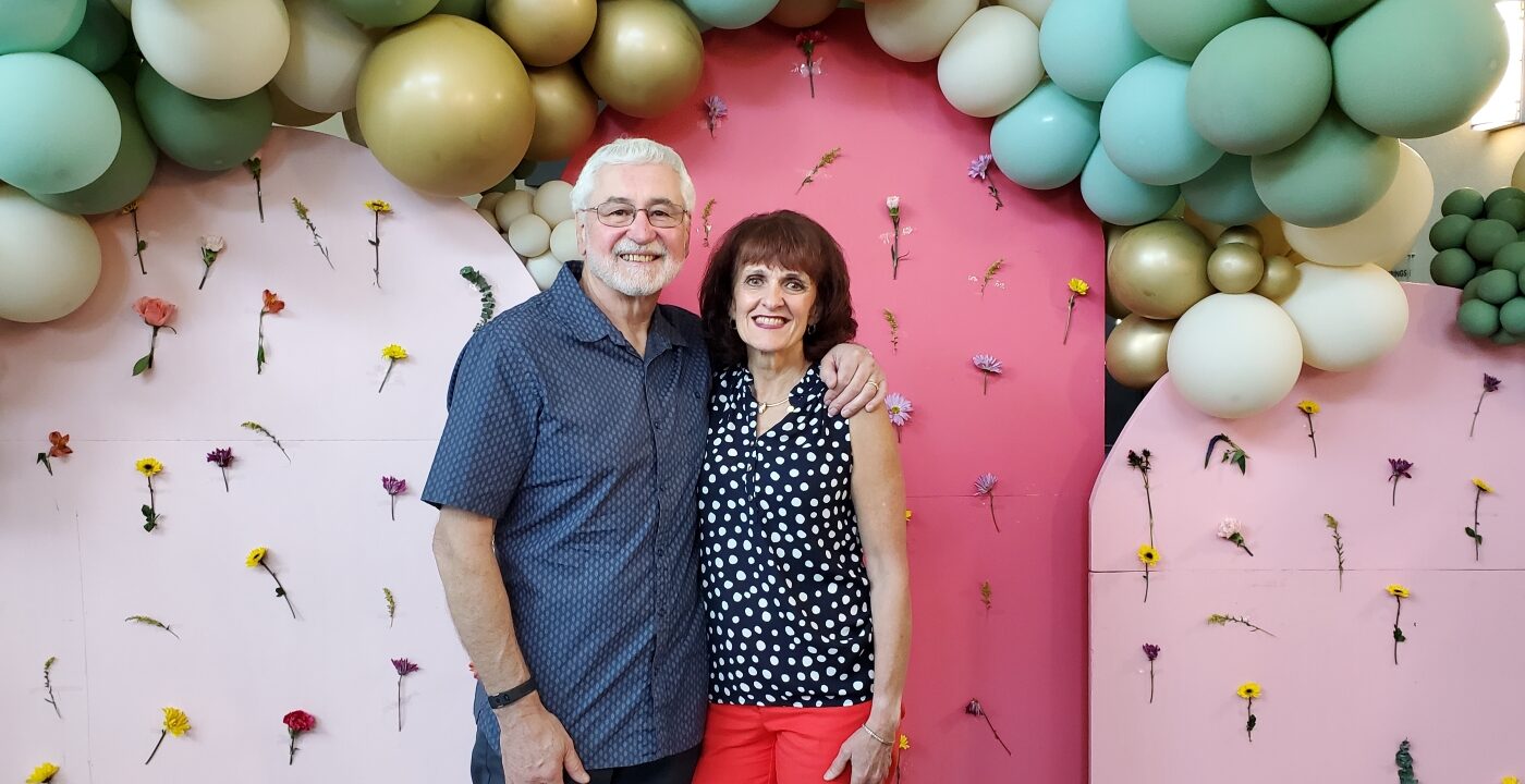 Man and woman stand underneath balloon arch