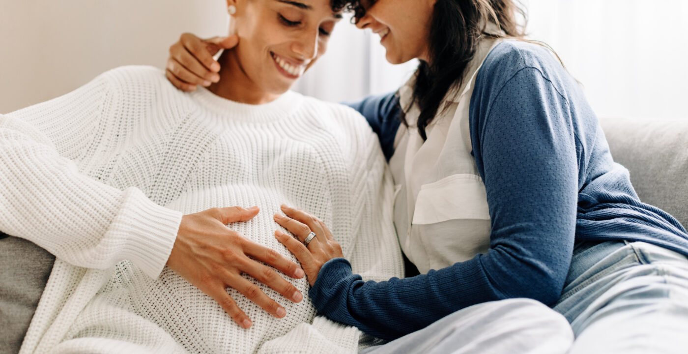 Two women smiling with hands on pregnant stomach