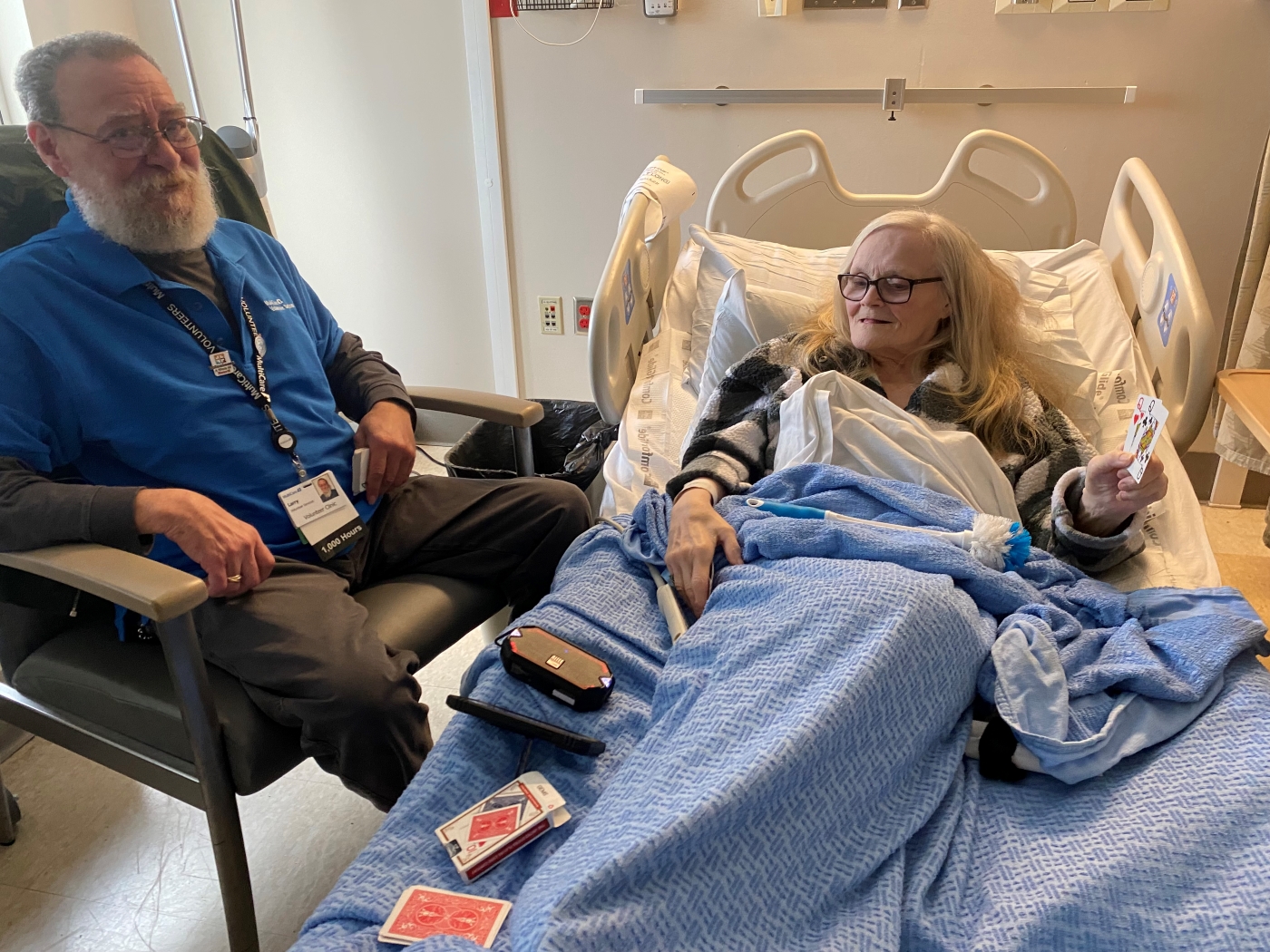 Woman in hospital bed and man sitting next to her play cards.