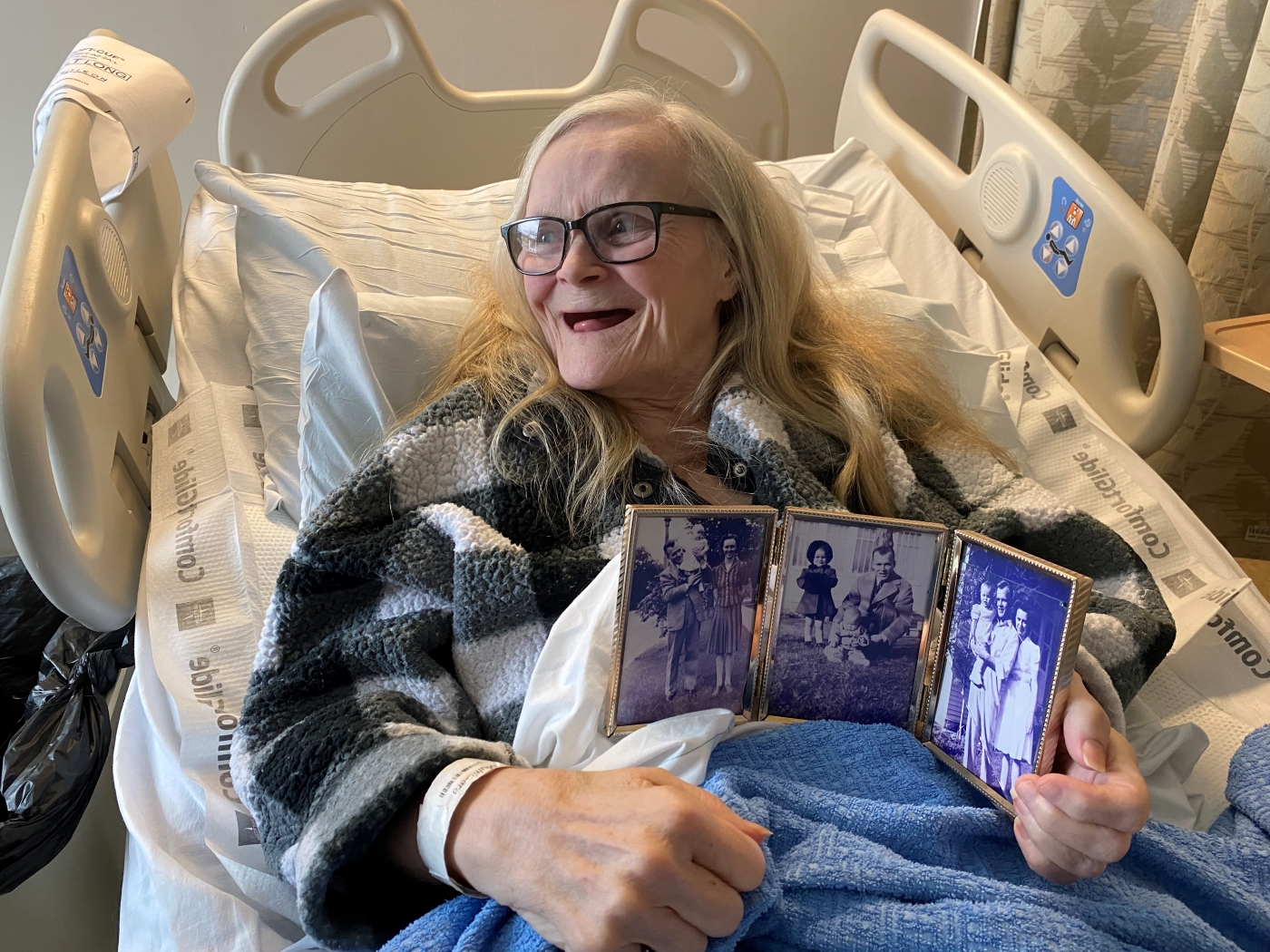 Woman in hospital bed holds framed photos and smiles