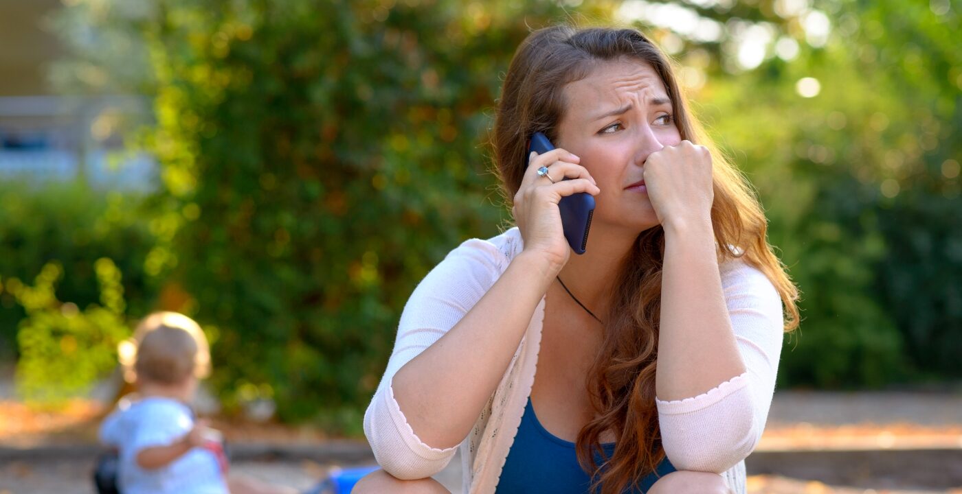 Parent in distress makes a phone call as toddler plays nearby