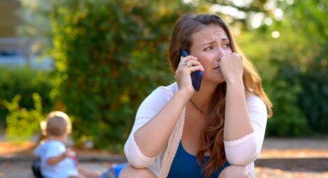 Parent in distress makes a phone call as toddler plays nearby