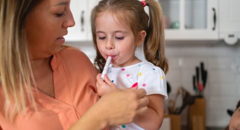 Mother holding toddler who is taking medication from a dosing syringe