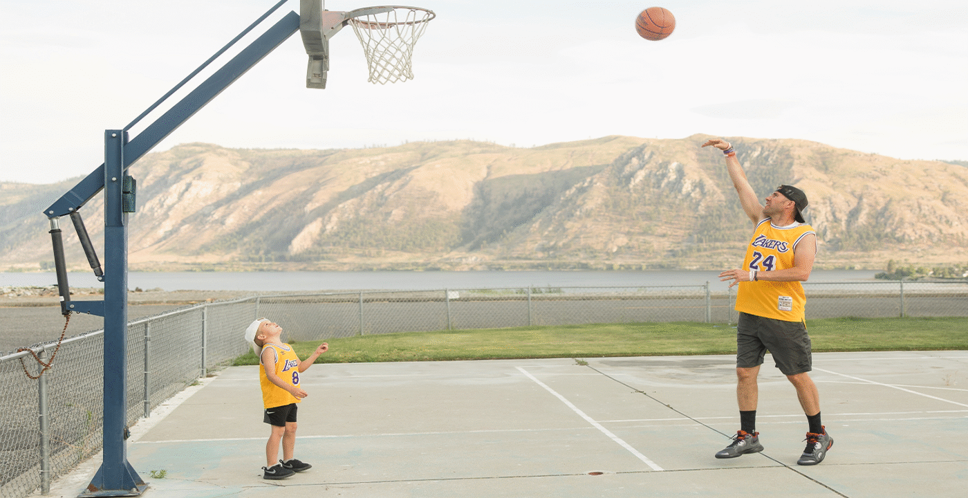 Man shooting basketball with child watching