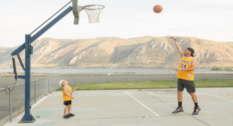 Man shooting basketball with child watching