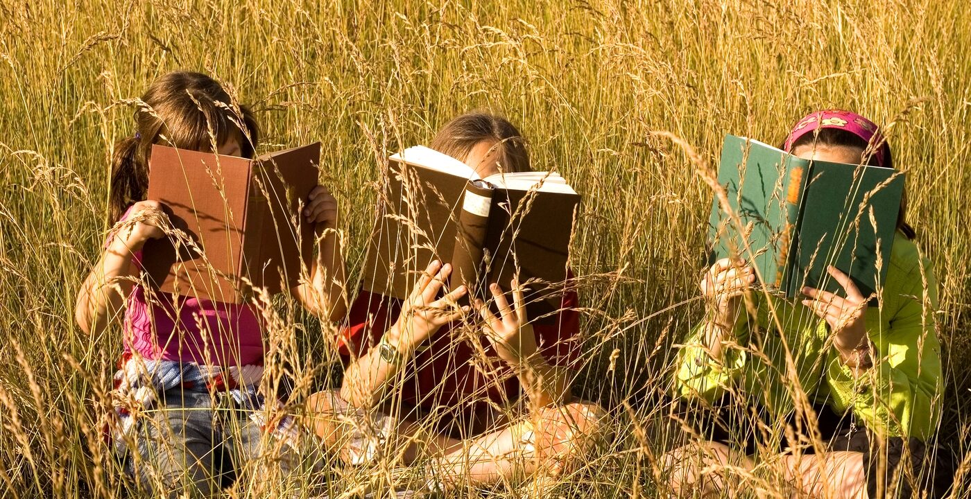 Three girls in a field, each with a book covering their face