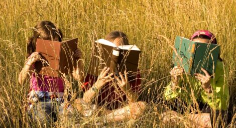 Three girls in a field, each with a book covering their face