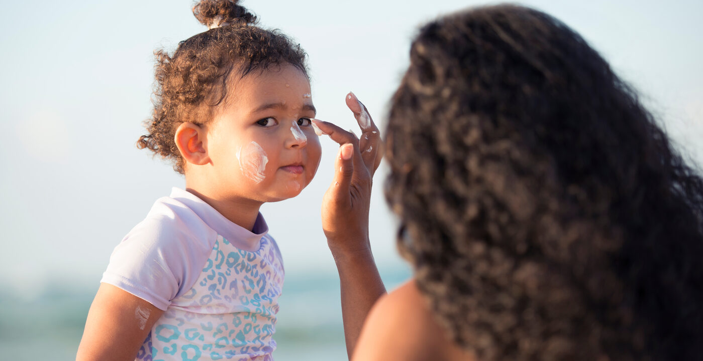 Mom applying sunscreen to child’s face on beach