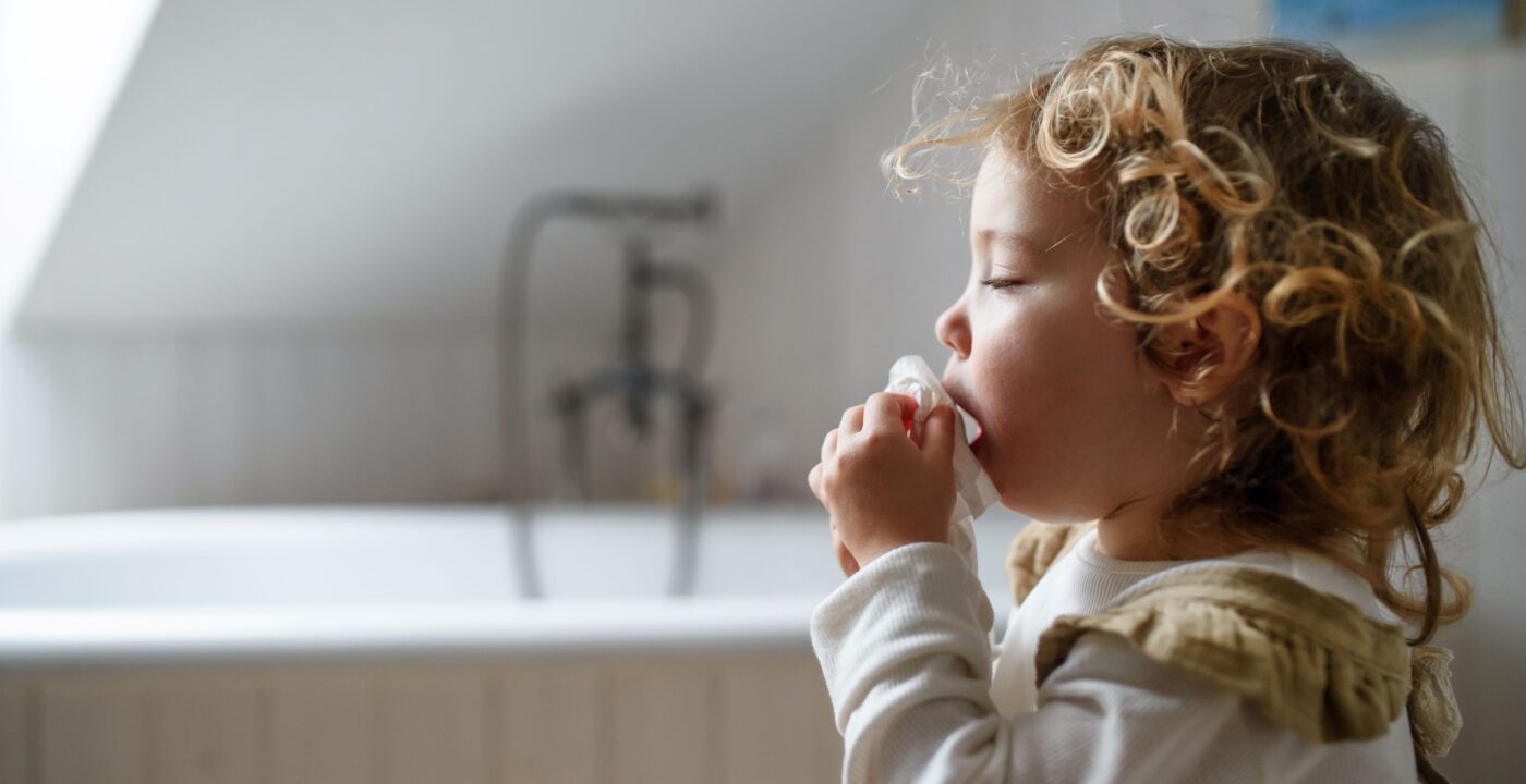 Sick toddler coughing into a tissue