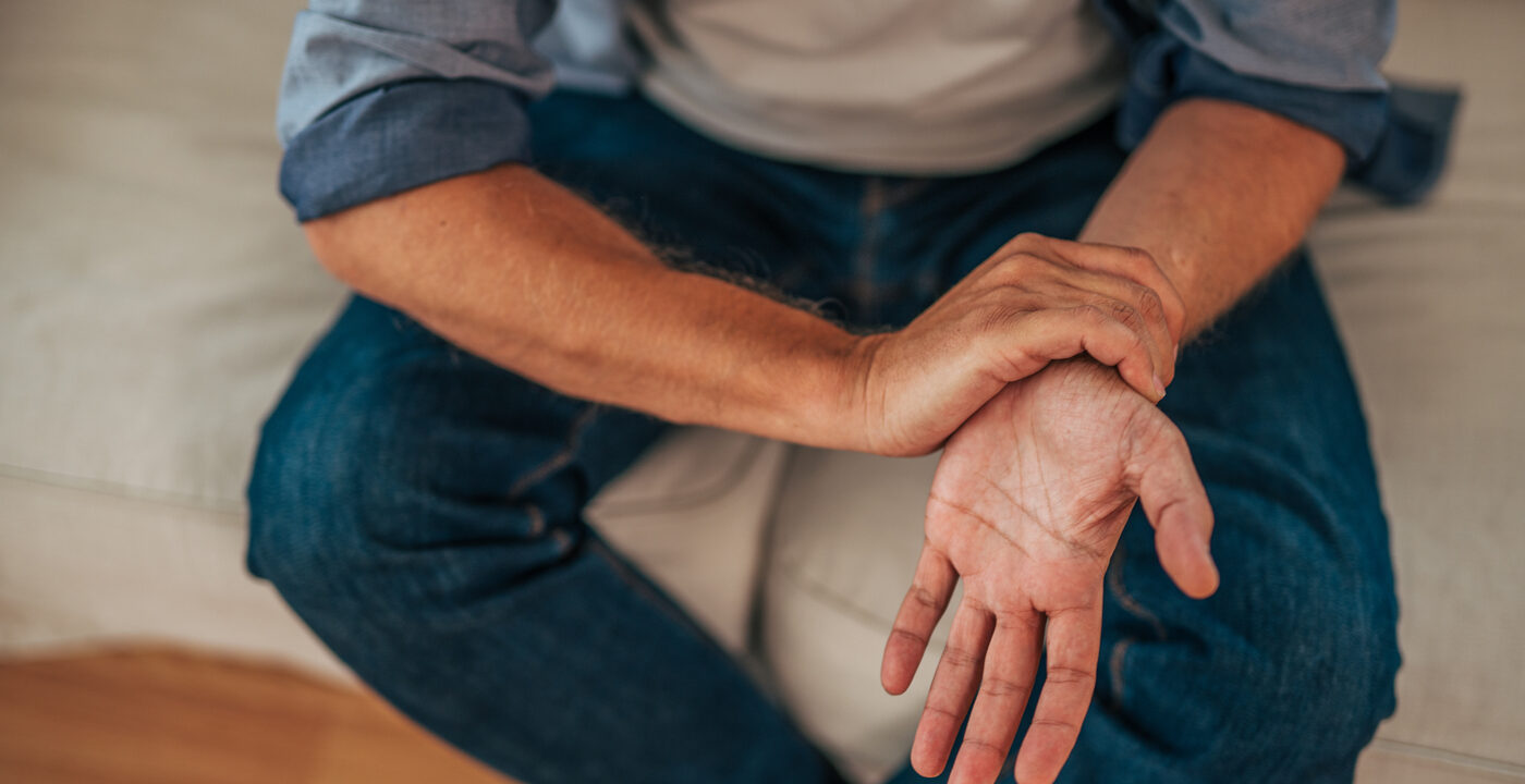 Man sitting on couch holding wrist with opposite hand