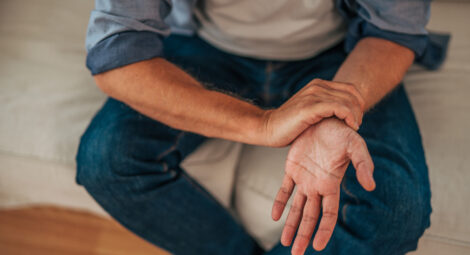 Man sitting on couch holding wrist with opposite hand