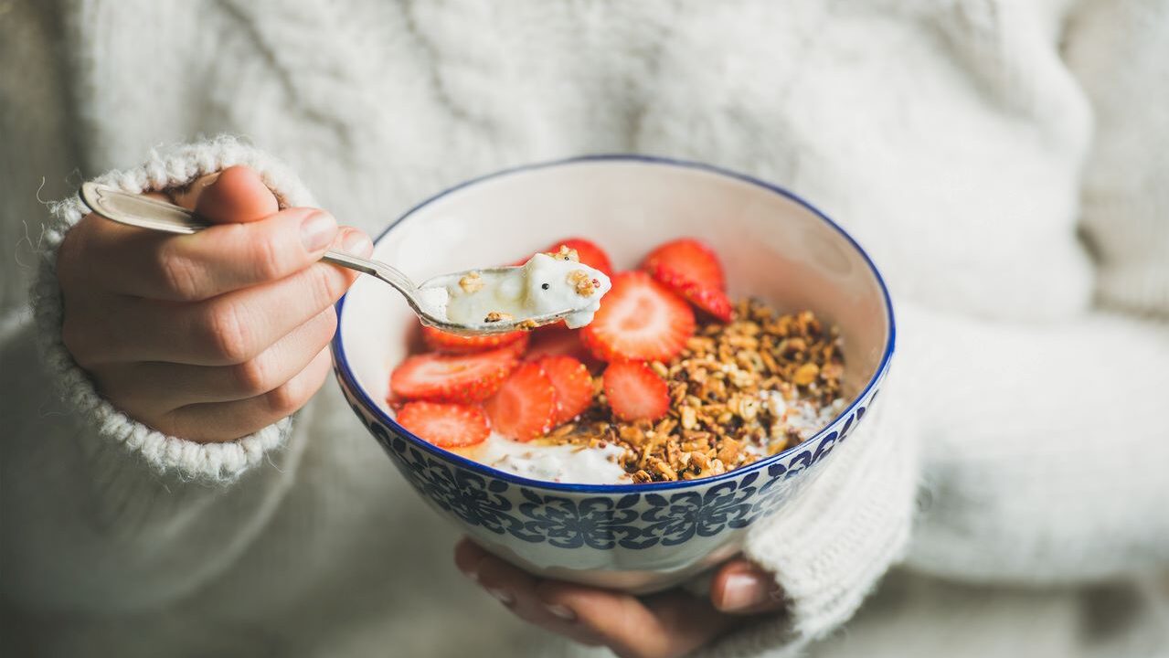 Person eating a bowl of granola, yogurt and fruit