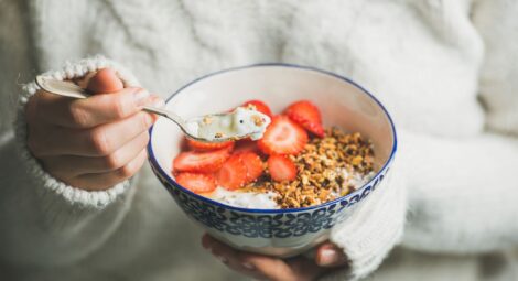Person eating a bowl of granola, yogurt and fruit