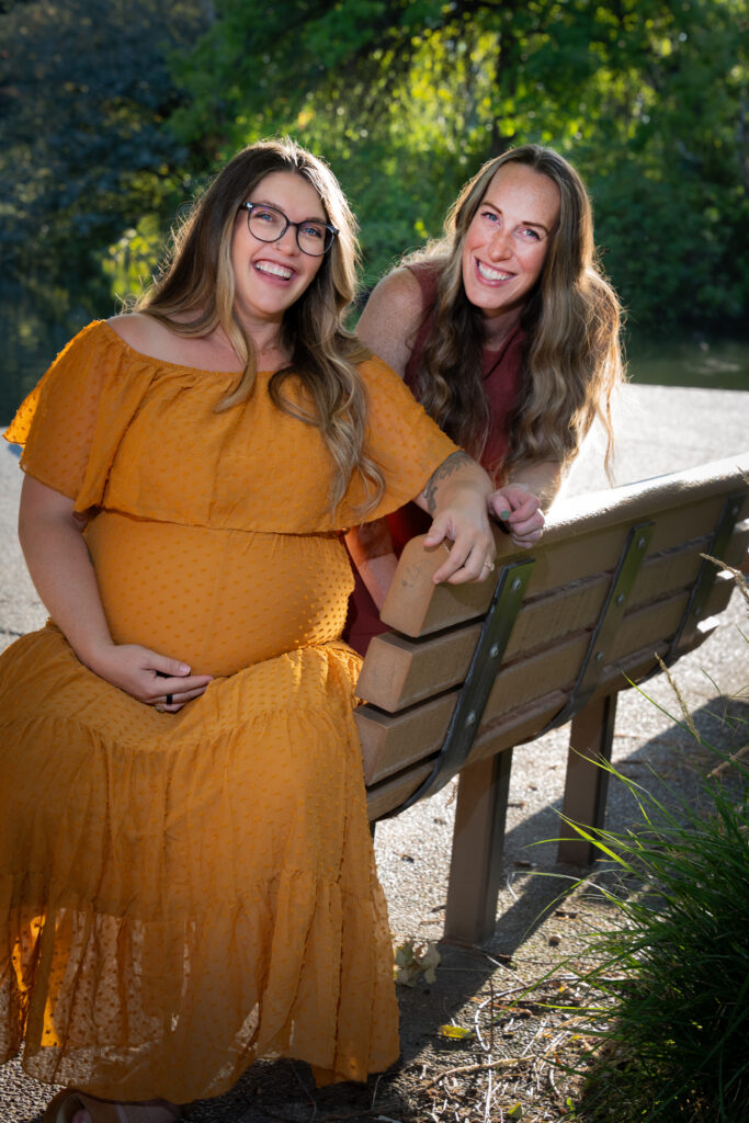 Pregnant woman and her friend sit on a bench.