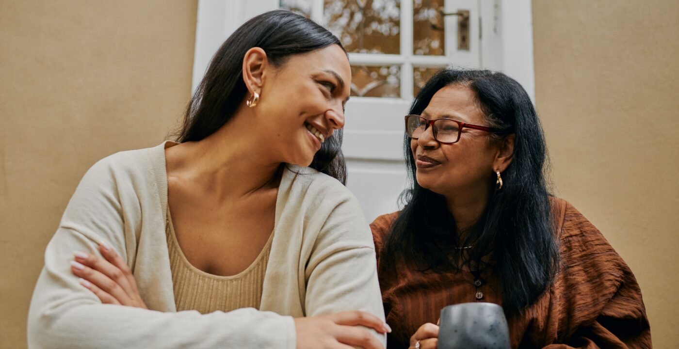 Mother and daughter sit together and smile on their front steps.