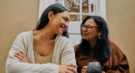 Mother and daughter sit together and smile on their front steps.