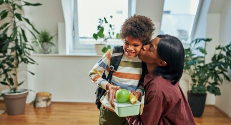 Child holding his lunch as his mom kisses him goodbye