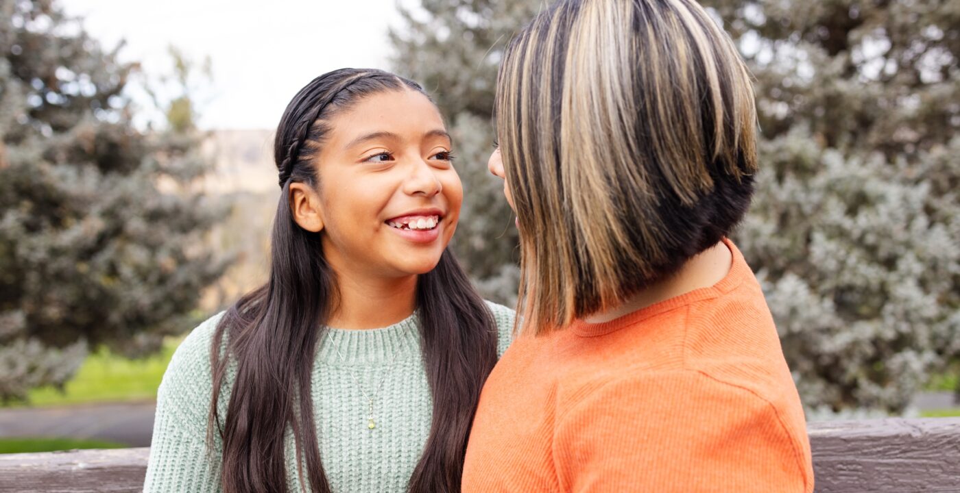 Young girl smiles at mom while sitting outside on a park bench