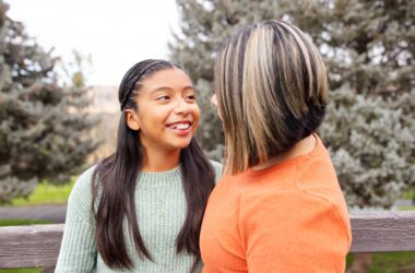 Young girl smiles at mom while sitting outside on a park bench