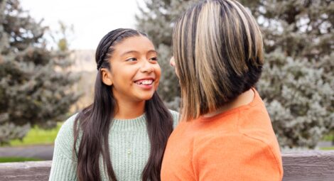 Young girl smiles at mom while sitting outside on a park bench