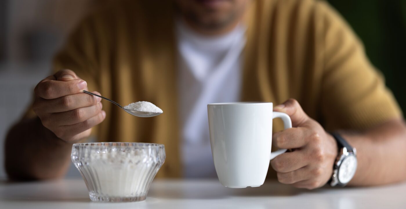 Man holding a spoonful of sugar and a coffee cup