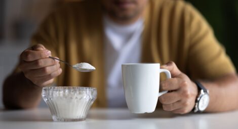 Man holding a spoonful of sugar and a coffee cup