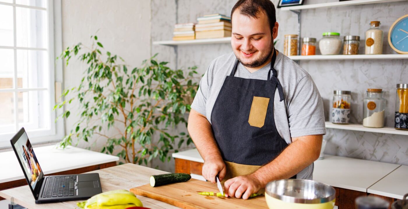 man wearing apron cutting a cucumber