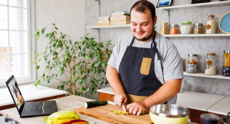man wearing apron cutting a cucumber