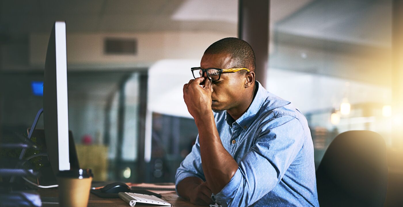 Stressed-out man sitting at desk pinching the bridge of his nose