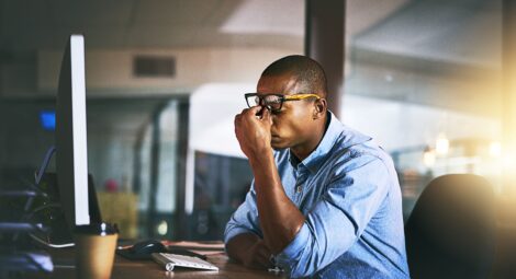 Stressed-out man sitting at desk pinching the bridge of his nose